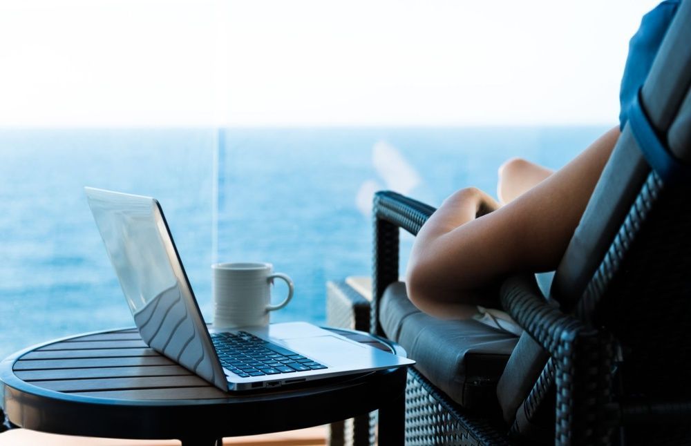 Laptop and coffee on a balcony table beside a reclining chair overlooking the ocean