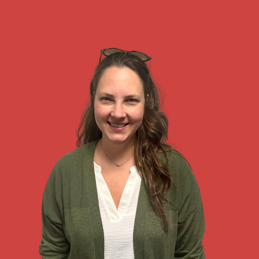 A woman wearing sunglasses and a green cardigan is smiling in front of a red background.