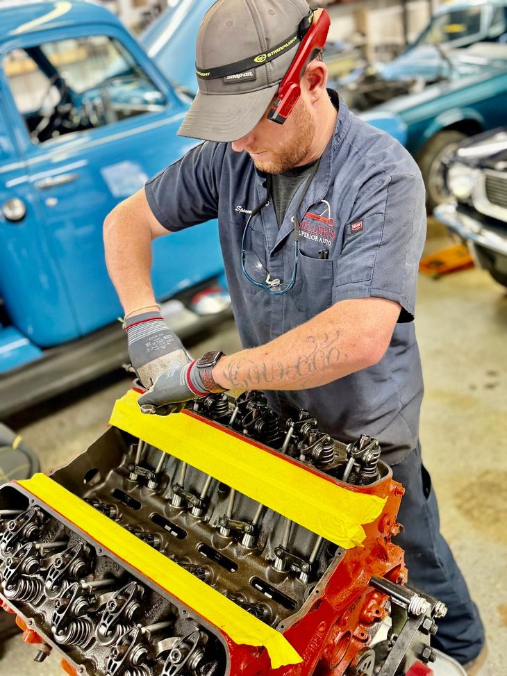Mechanic working on a car engine with a yellow support bar in a garage