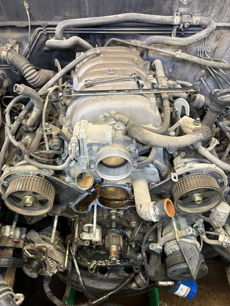 Car engine bay with exposed intake, belts, hoses, and wiring, viewed from above.