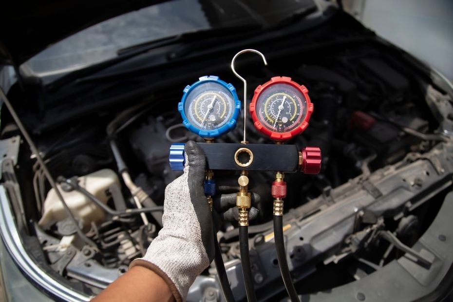 Gloved hands holding red and blue AC manifold gauges over an open car engine bay
