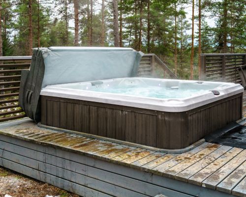 A hot tub is sitting on a wooden deck in the woods.