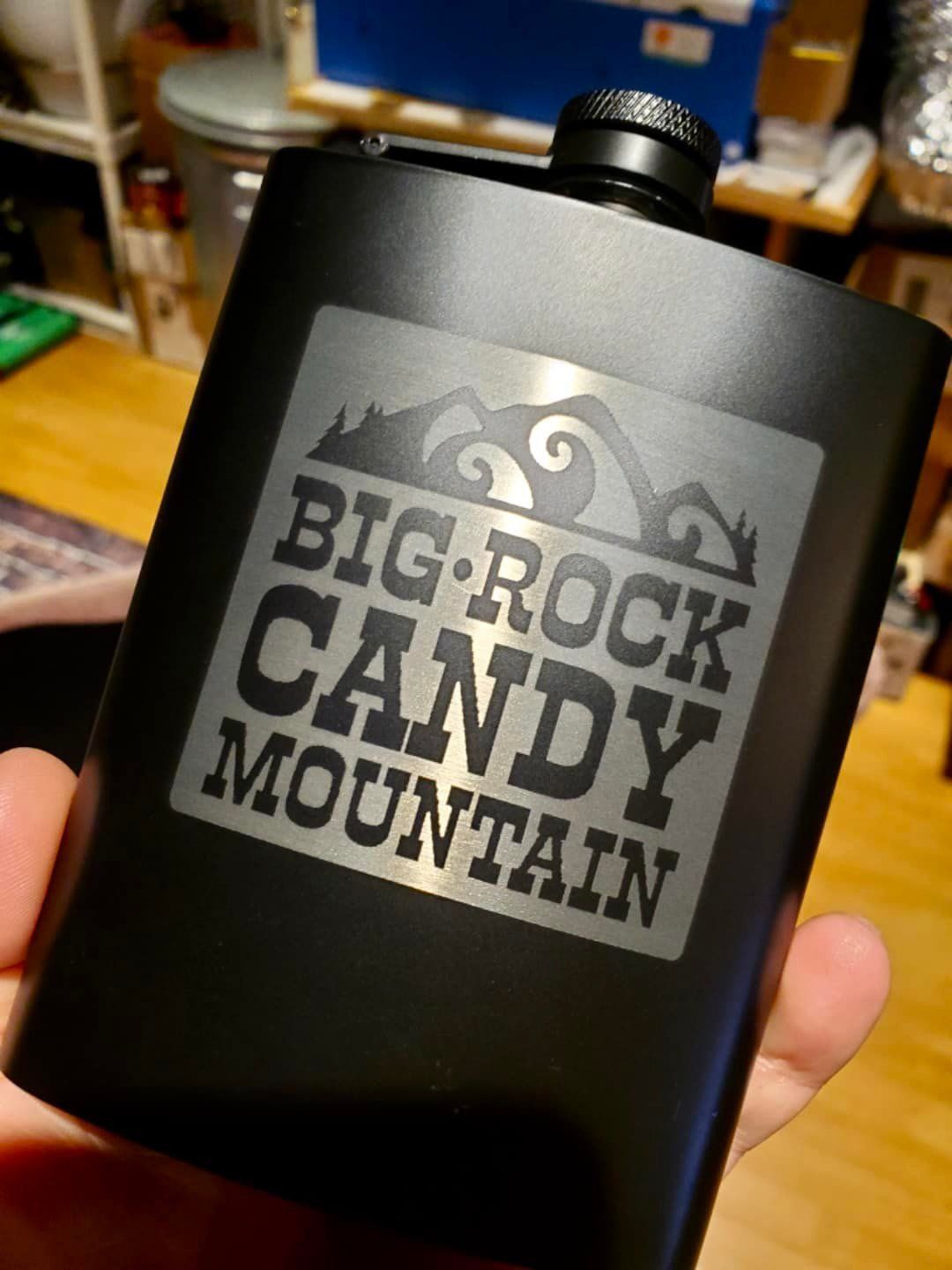 A person is holding a flask that says big rock candy mountain