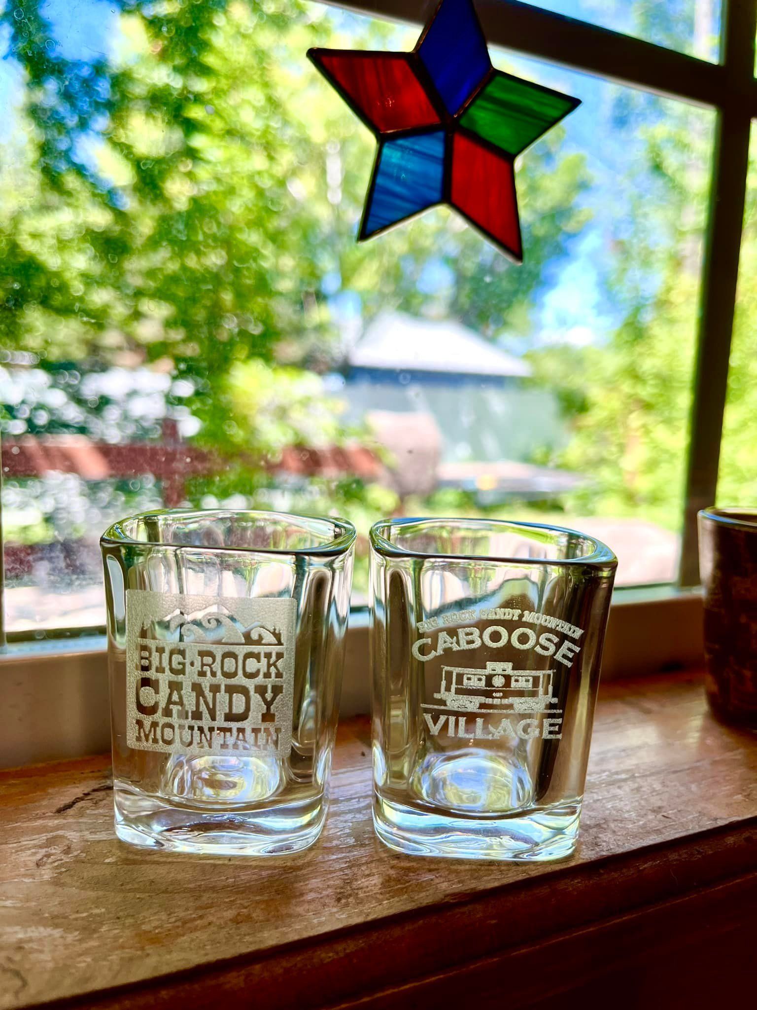 Two shot glasses are sitting on a window sill next to a stained glass star.