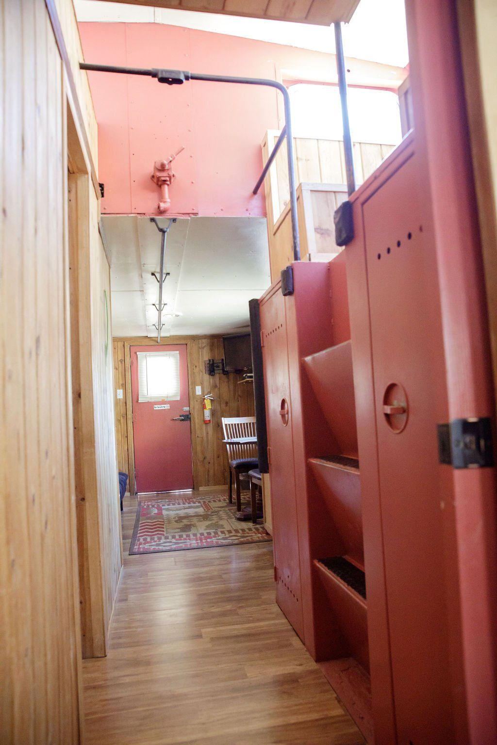 A hallway in a house with a red door and stairs leading up to the second floor.
