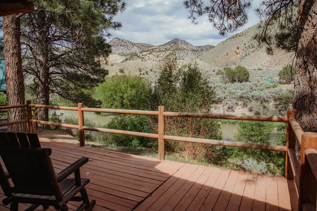 A wooden deck with chairs and a fence overlooking a mountain range.