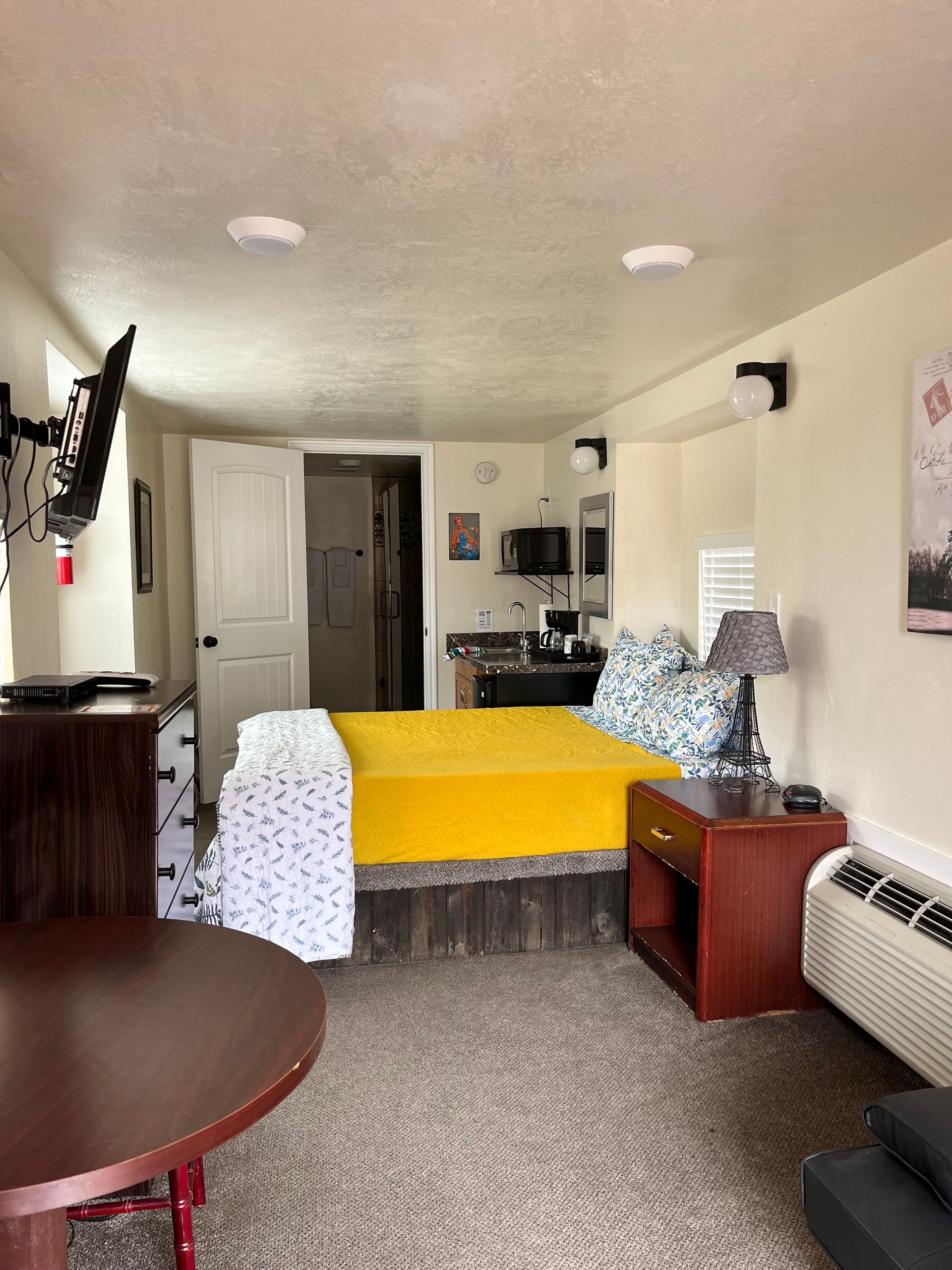 A hotel room with a bed , nightstand , table and television.