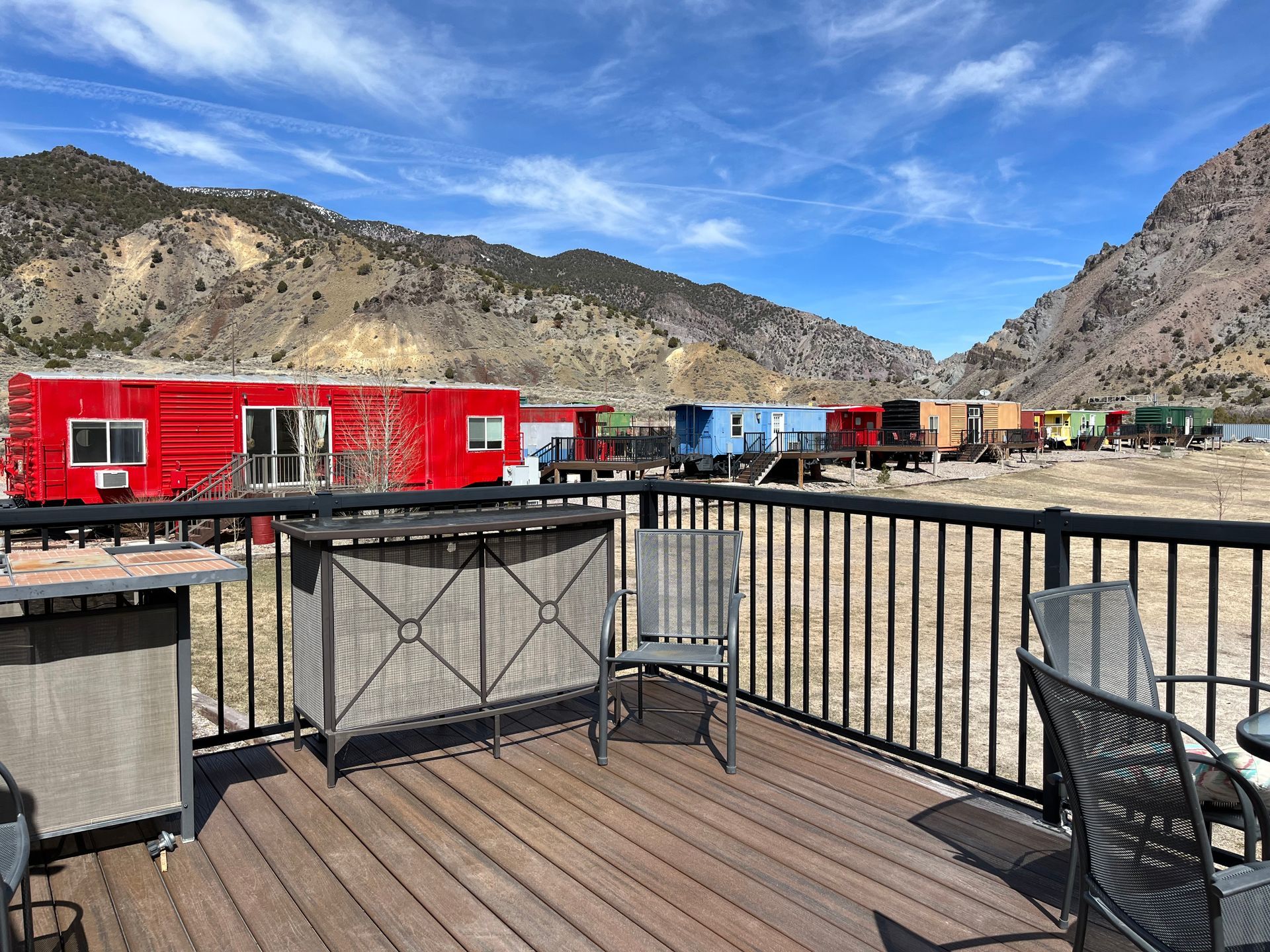 A deck with a railing and chairs and a red trailer in the background.