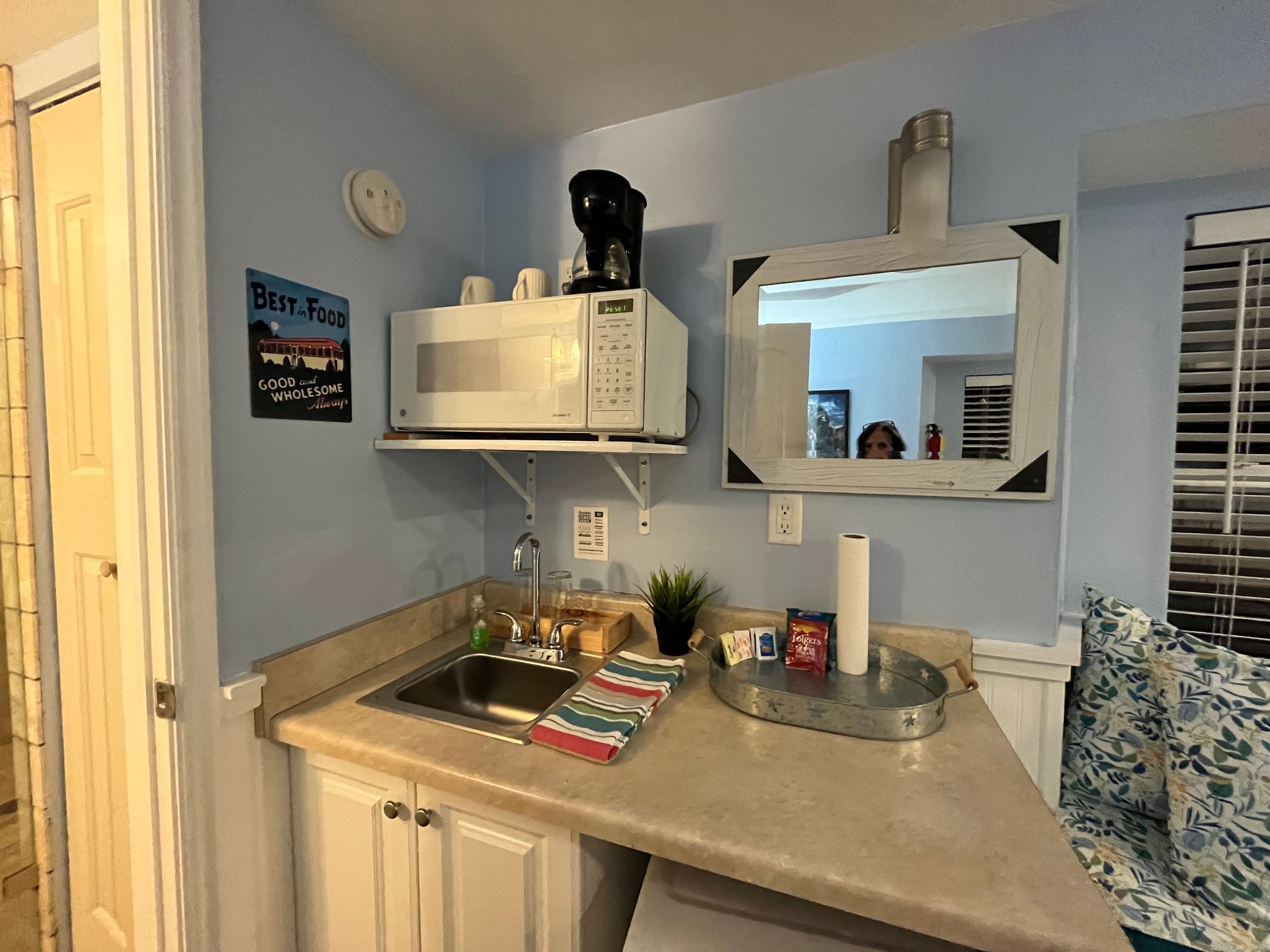 A kitchen with a sink , microwave and mirror