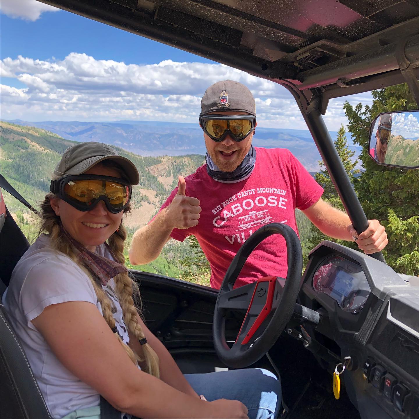 A man and a woman are sitting in a vehicle giving a thumbs up.