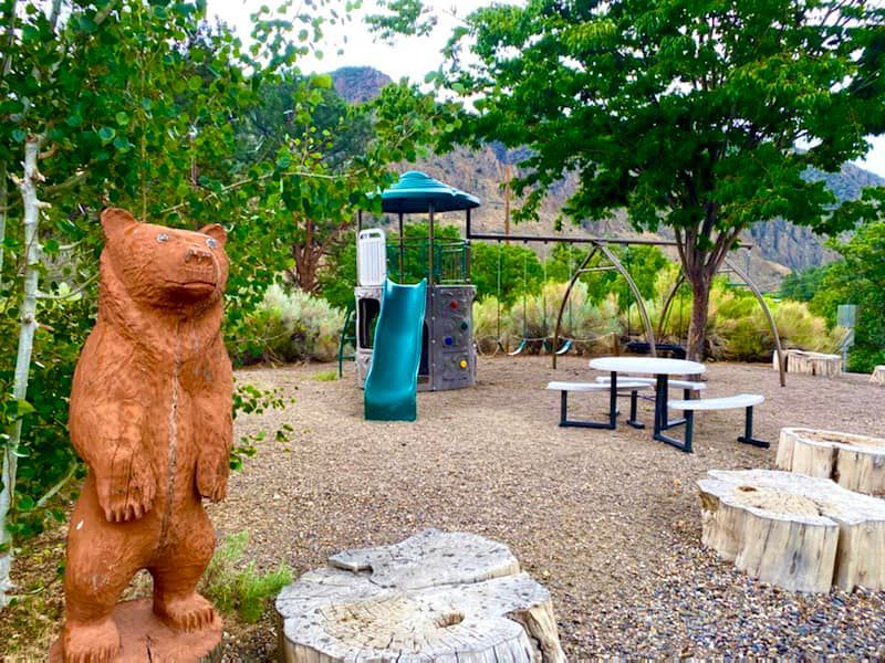 A statue of a bear is standing in front of a playground.