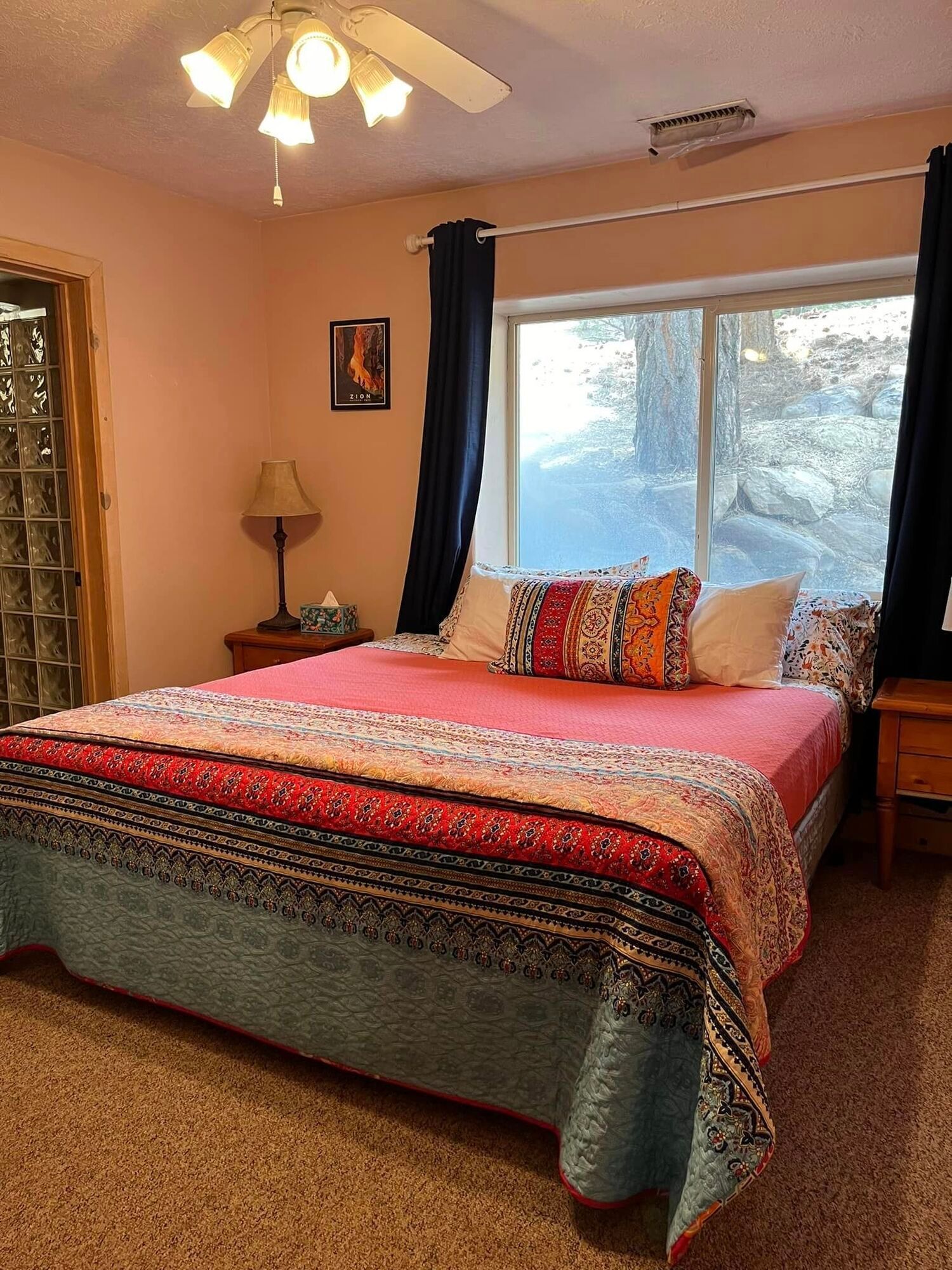 A bedroom with a large bed , a ceiling fan , a mirror and a window.