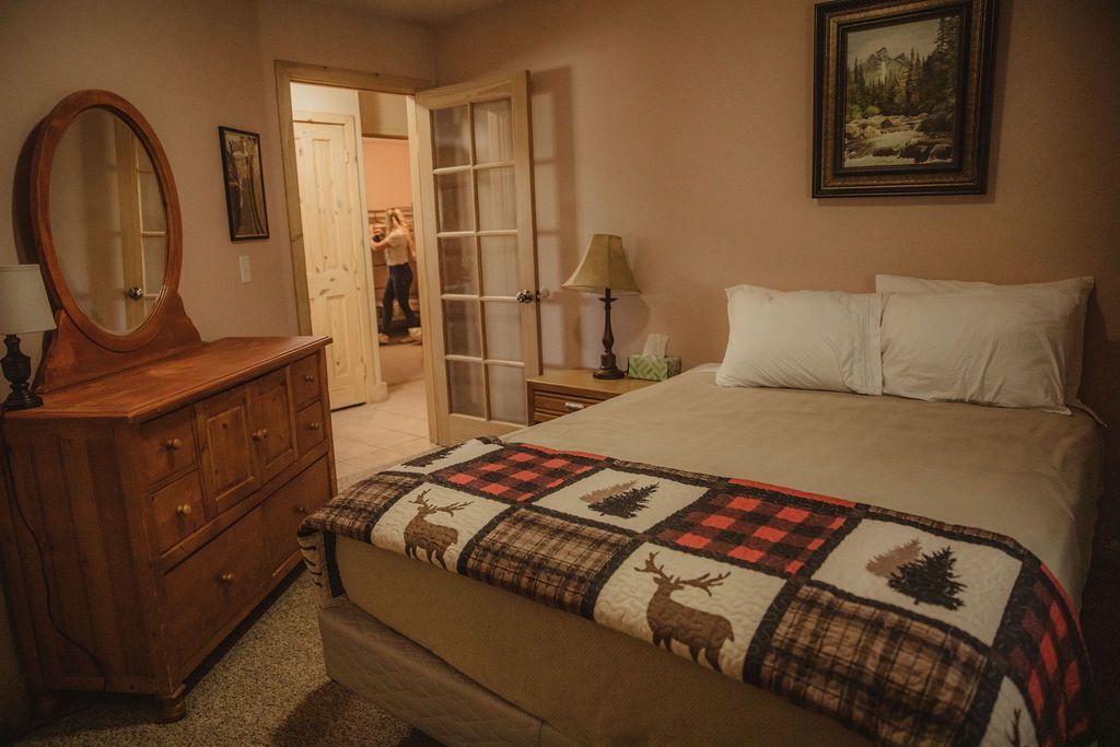 A bedroom with a bed , dresser , mirror and lamp.