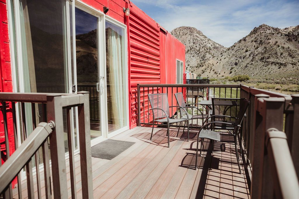 A red house with a wooden deck and mountains in the background.