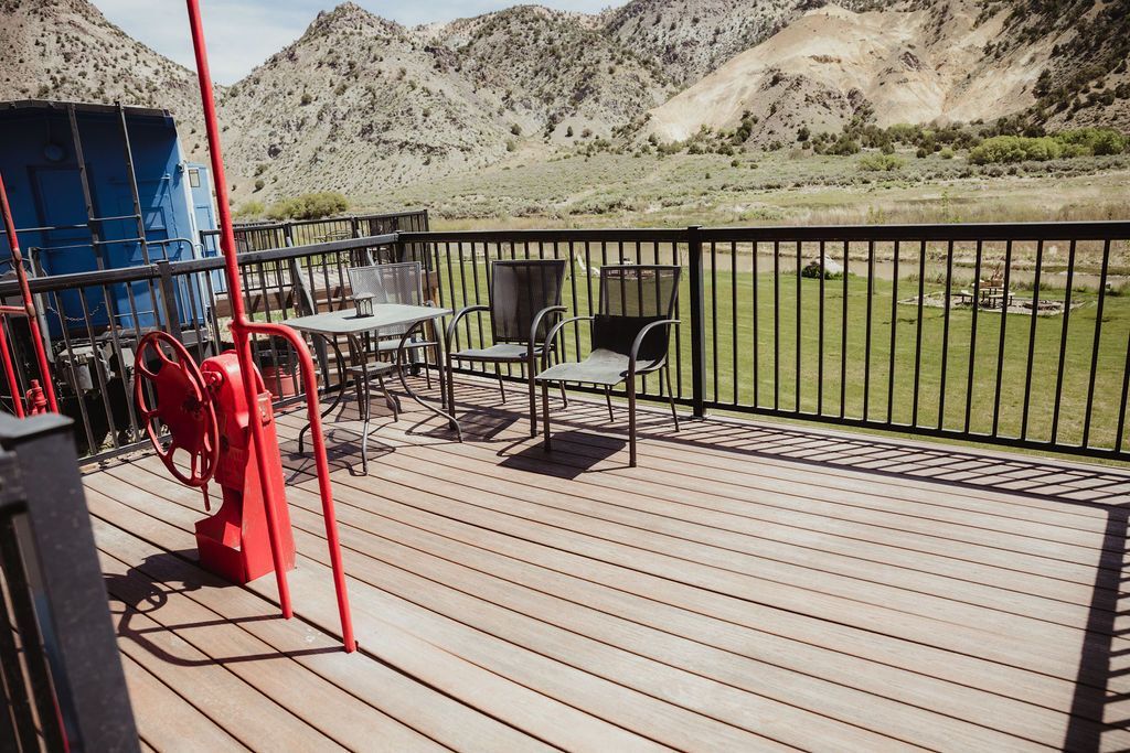 A wooden deck with a metal railing and chairs.