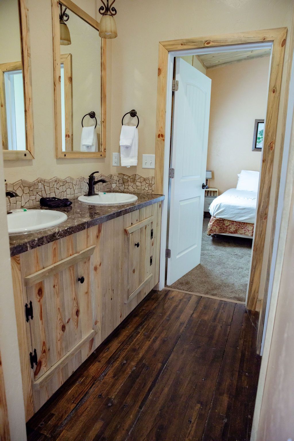 A bathroom with two sinks and two mirrors and a door leading to a bedroom.
