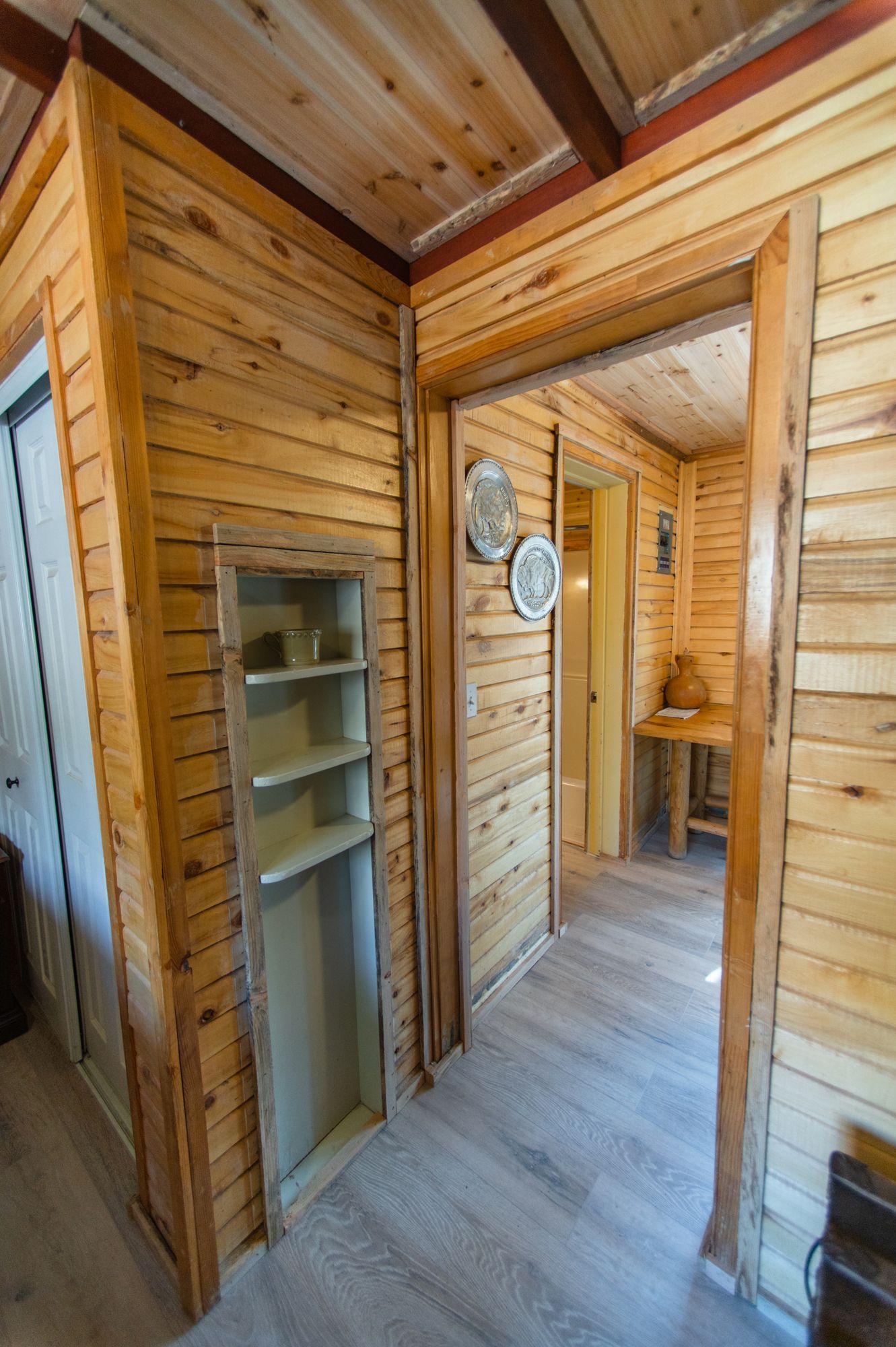 A hallway in a wooden cabin with a doorway leading to a room.