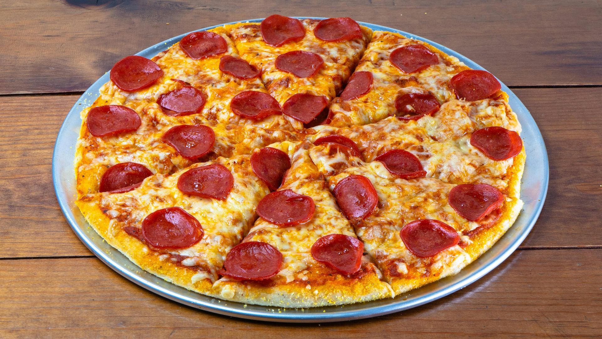 A pepperoni pizza is sitting on a metal pan on a wooden table.