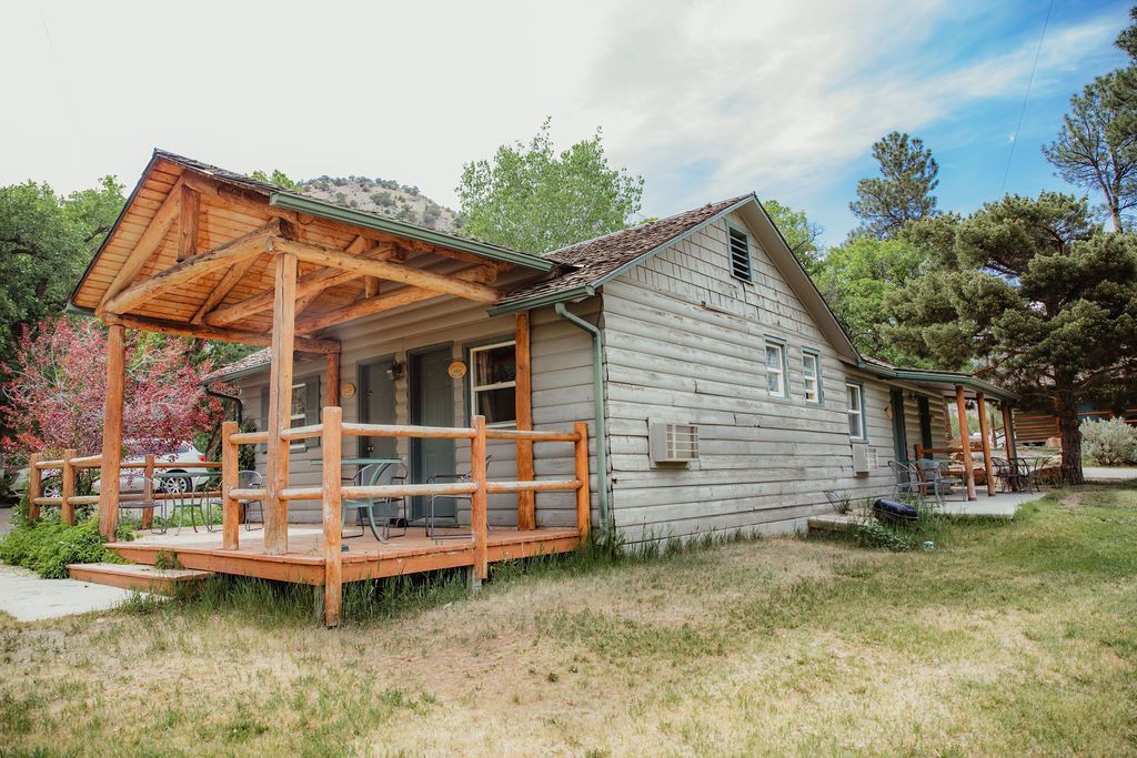 A small white house with a wooden porch and a fence in front of it.