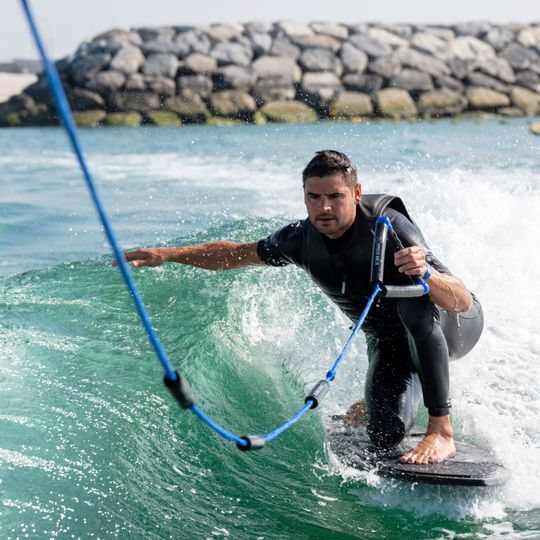 Wakeboarder in a lifejacket carving through water, holding a blue tow rope