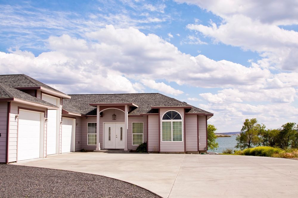 Single-story house with garage, concrete driveway, and a lake view under a cloudy sky