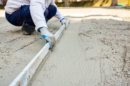Worker smoothing wet concrete with a trowel at a construction site