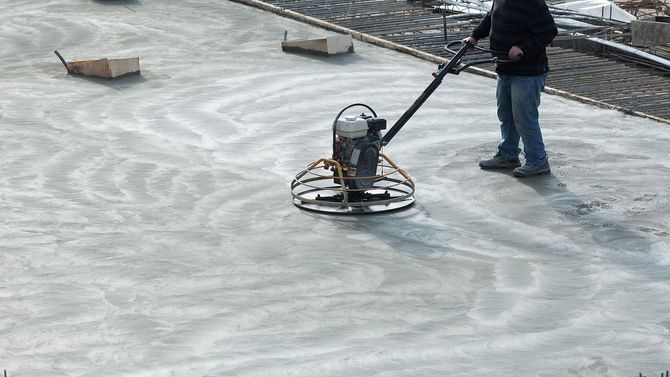 Worker using a power trowel to smooth a concrete slab outdoors