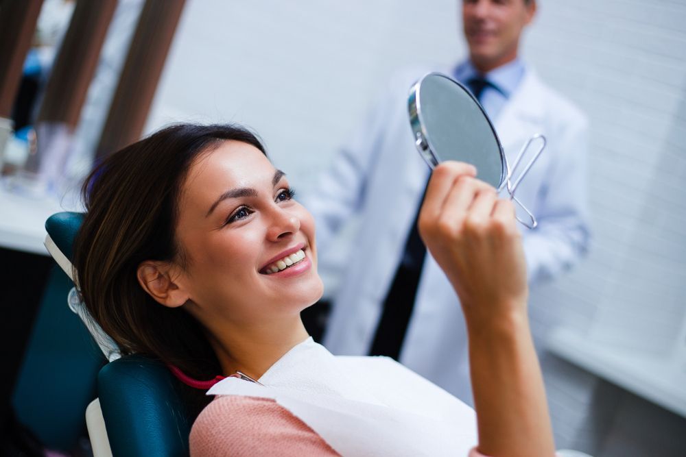 Smiling Dental Patient Holding a Mirror While a Dentist Stands in the Background — Mareeba Dental Centre in Mareeba, QLD