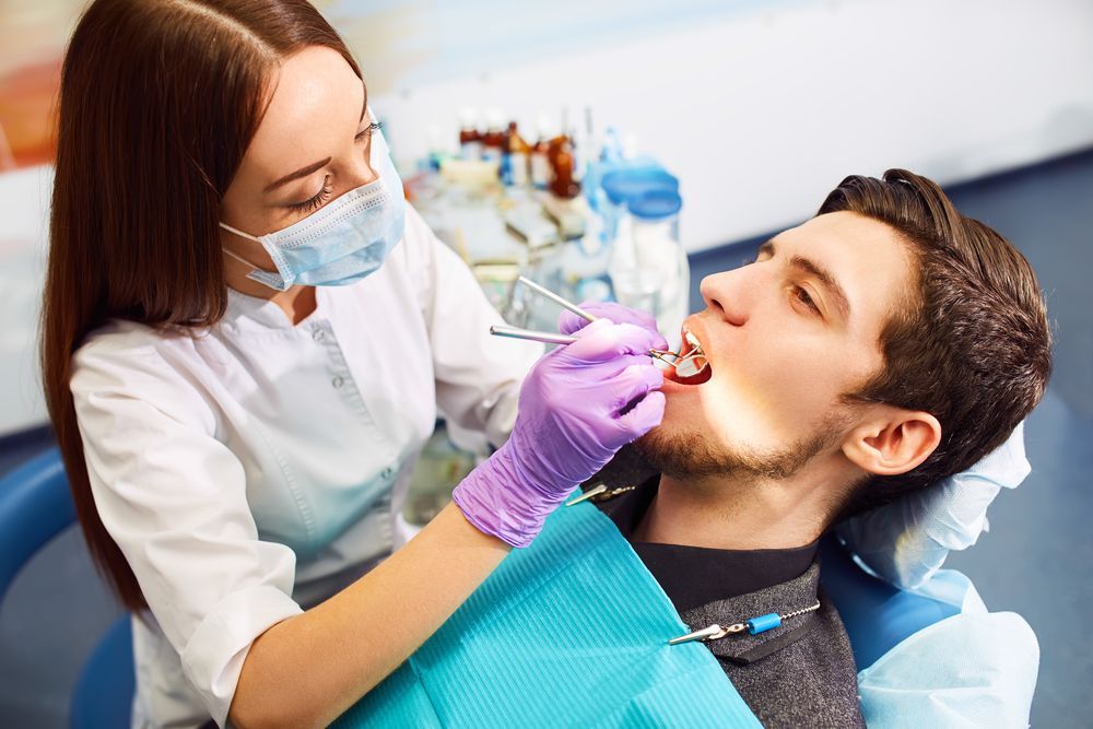 A Dentist in a White Coat and Blue Mask Examines a Patient's Teeth — Mareeba Dental Centre in Mareeba, QLD