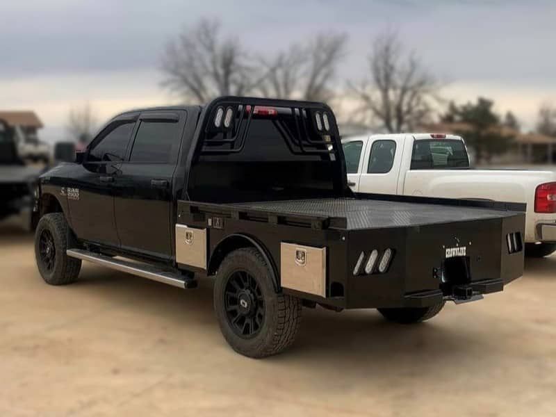 a black truck with a flat bed is parked in a dirt lot .