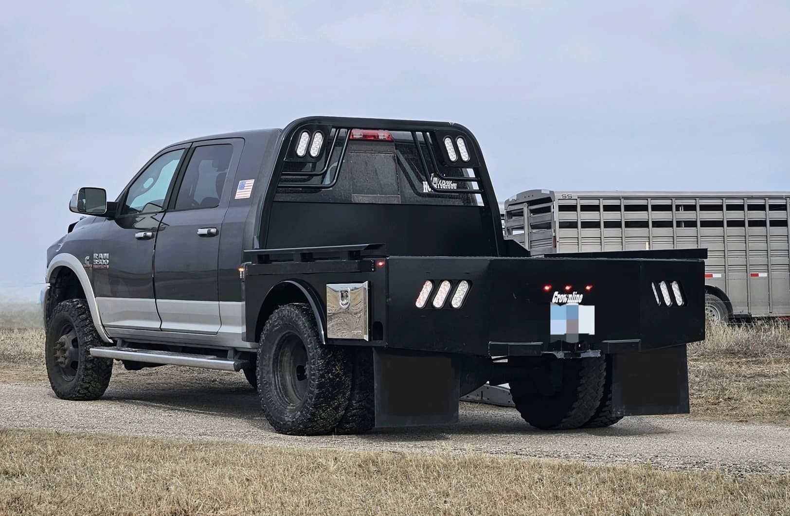 A black ram mega cab truck with a skirted flat bed with toolboxes is parked in a field.