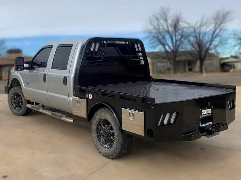 a silver ford 4 door truck with a flatbed is parked in a dirt lot .