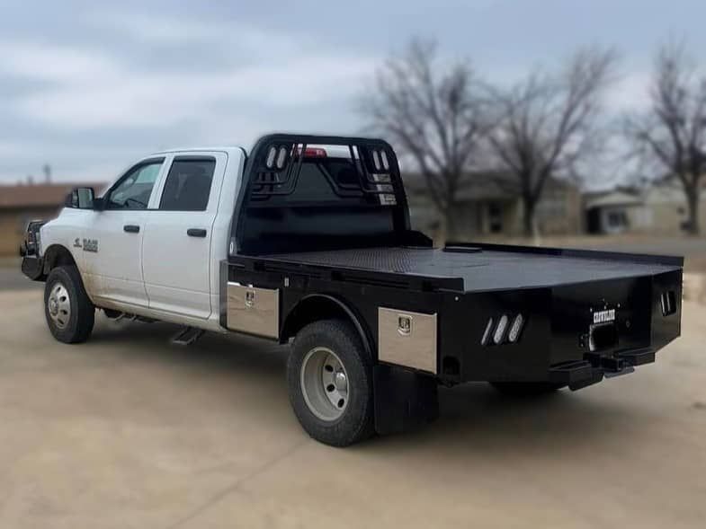 a white truck with a flatbed is parked on a dirt road .