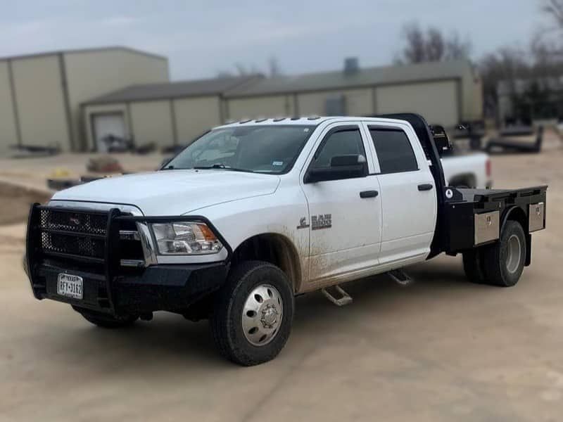 a white truck with a flat bed is parked in a dirt lot .
