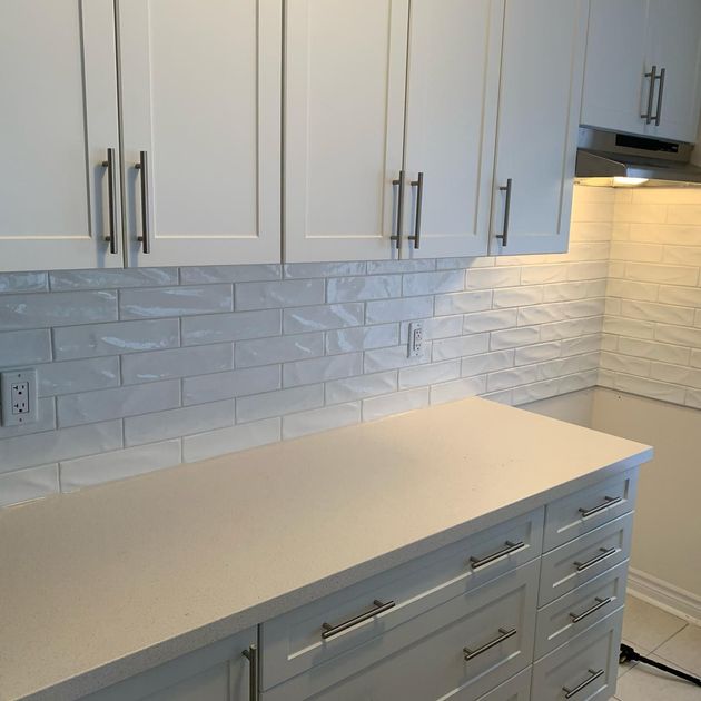 A modern kitchen with a white island, stainless beer keg, and dark wood flooring.