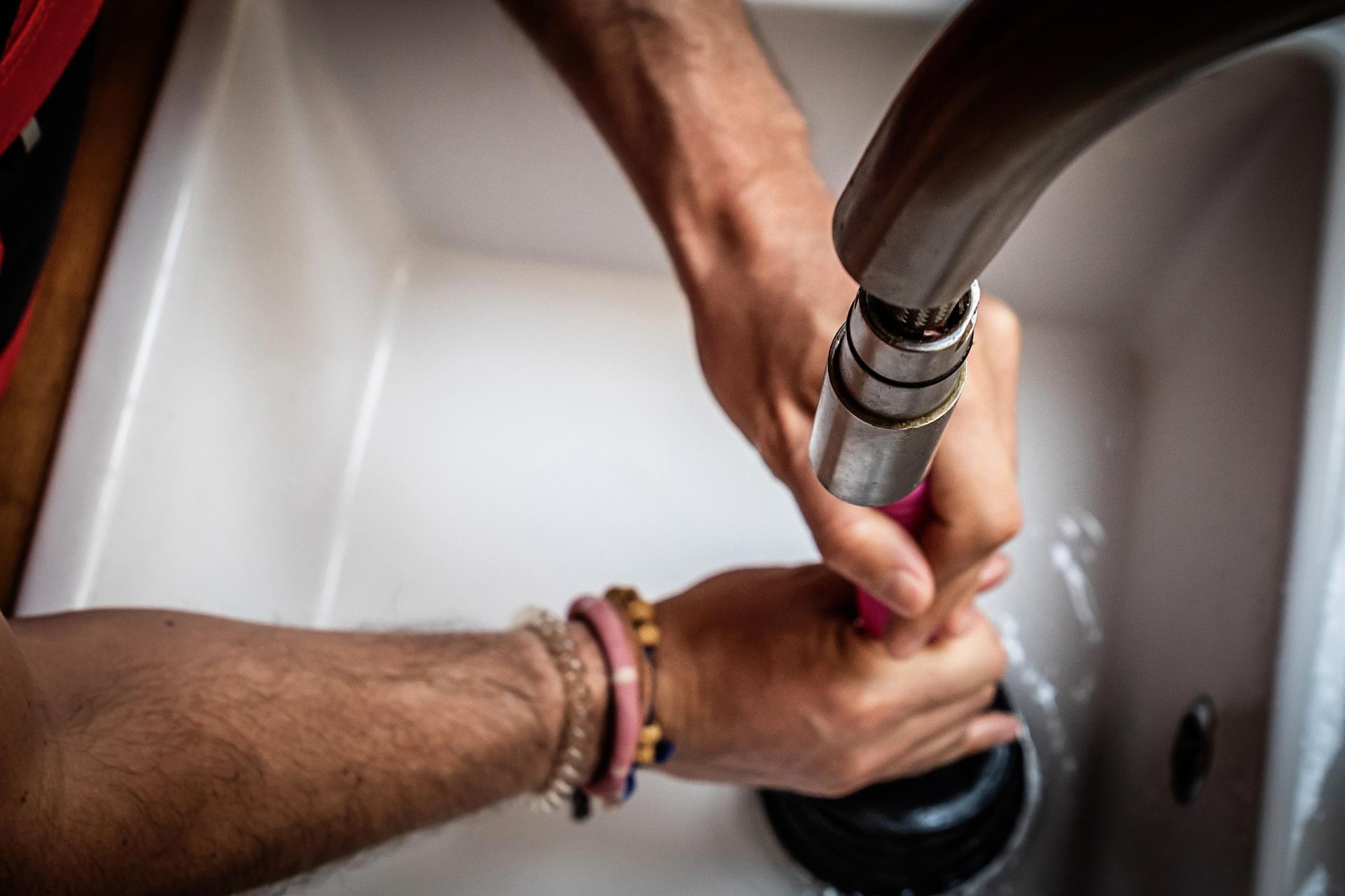 Hands using a plunger in a white sink, water present.