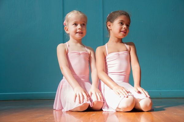 Two young dancers in pink leotards kneel on a wooden floor, smiling and looking to the side — Kay Flynn Dancing Academy Southport in Southport, QLD