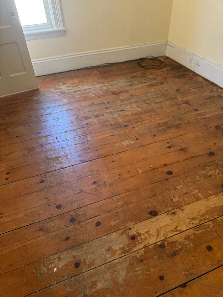 Empty room with worn wooden floorboards and a window letting in light