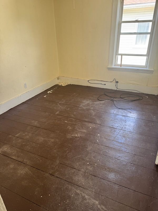 Empty room with worn dark wood floor, pale yellow walls, and a window with visible cords