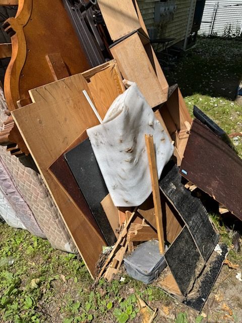 Pile of broken wooden panels, a white cloth, and scrap boards leaning outdoors on grass.