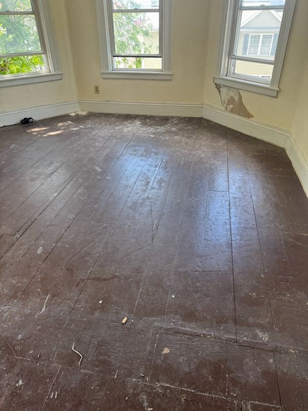 Empty room with worn dark wood floor and large windows letting in daylight