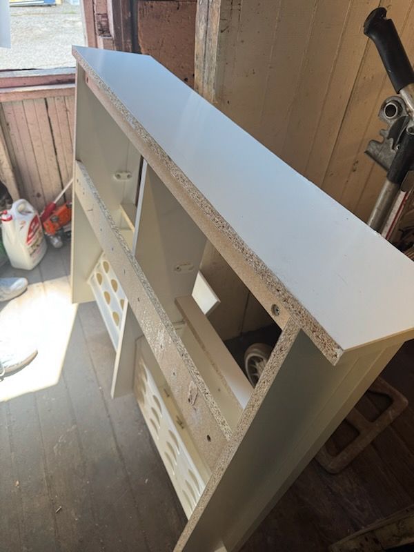 White bathroom vanity cabinet with open shelves in a workshop or garage setting