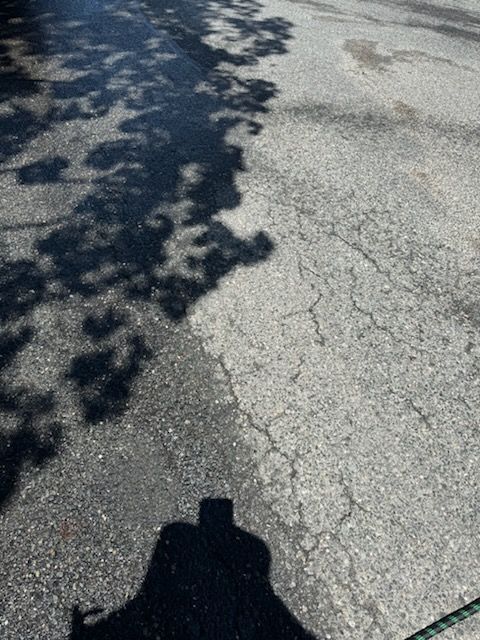 Shaded cracked asphalt road with tree shadows and a person’s shadow at the bottom edge