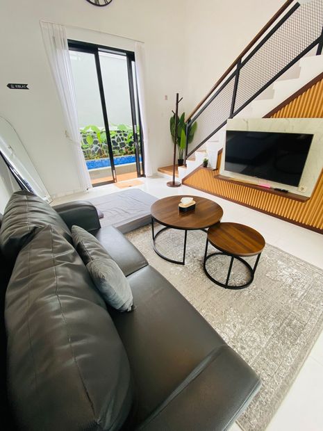 Modern living room with gray sofa, round coffee tables, wall-mounted TV, staircase, and open patio doors
