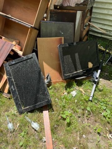 Broken furniture and wooden panels scattered on grass beside a building wall
