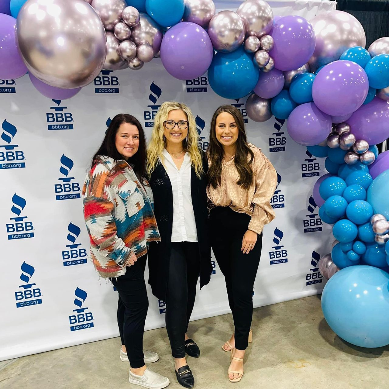 Three women smiling in front of a backdrop with balloons.