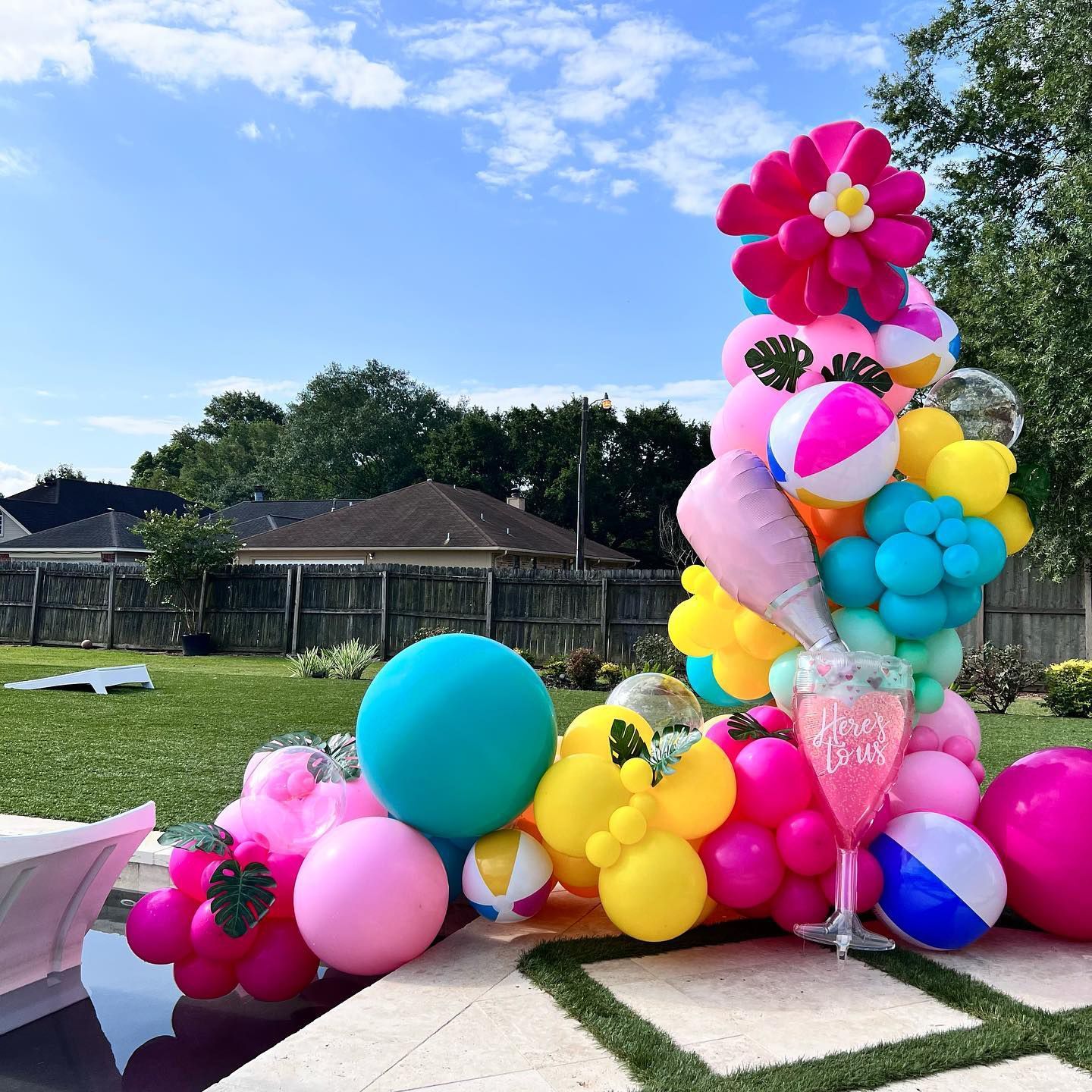 Colorful balloon arch with beach balls, flowers, and a drink by a pool.