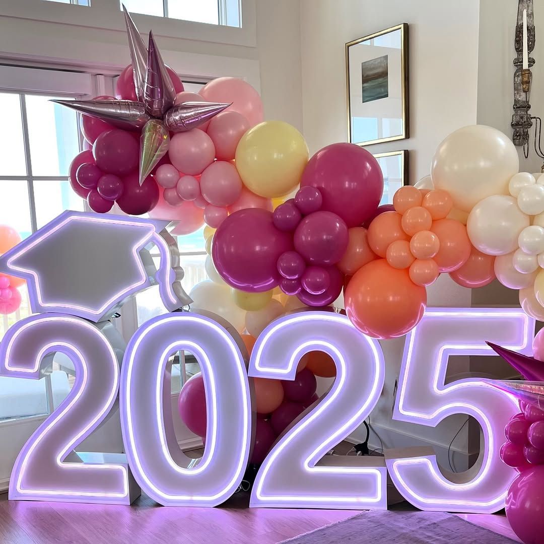 Outdoor event with balloon arch, tables, people, and building with palm trees.