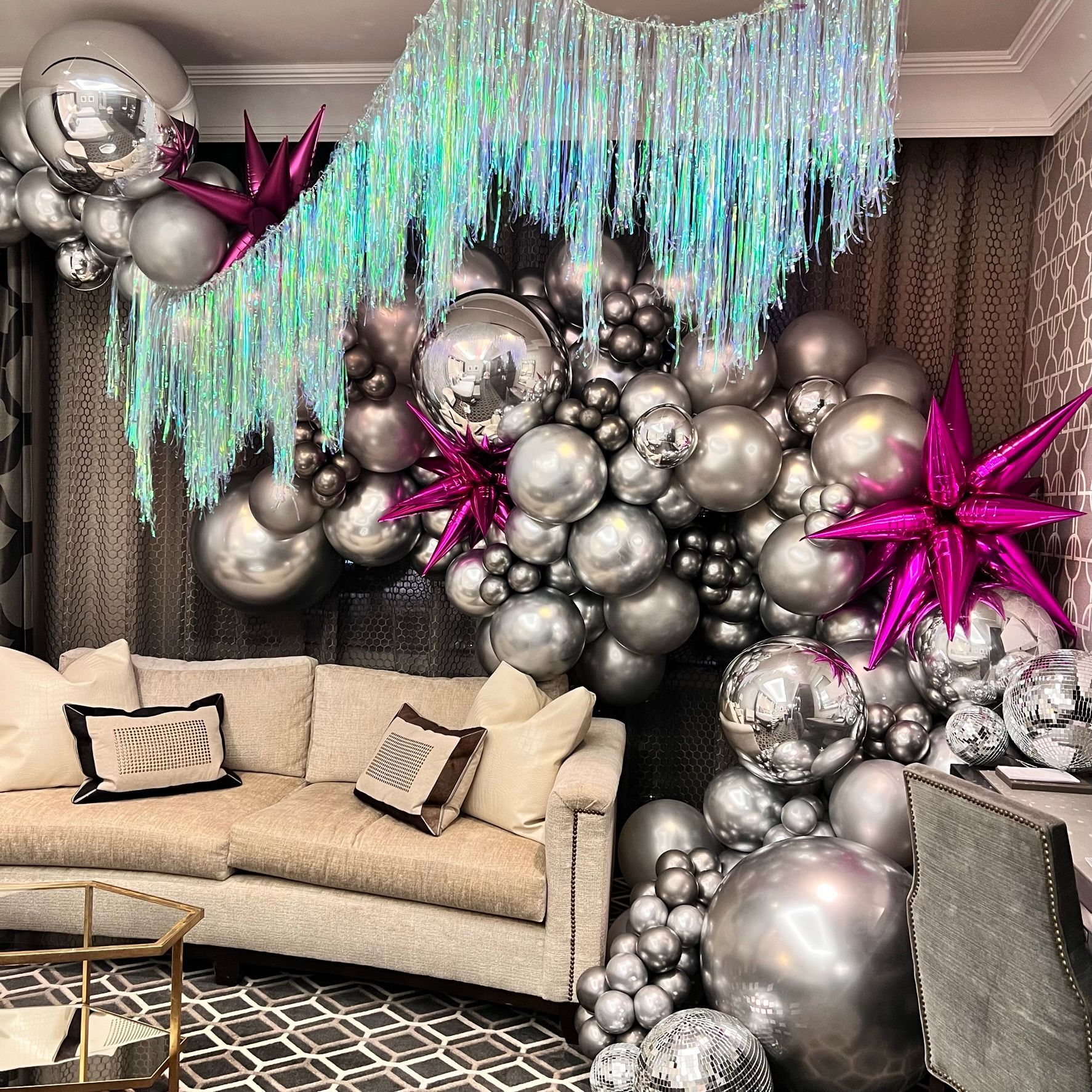 Silver balloons, fuchsia stars, and disco balls decorate a room with a fringed backdrop and couch.