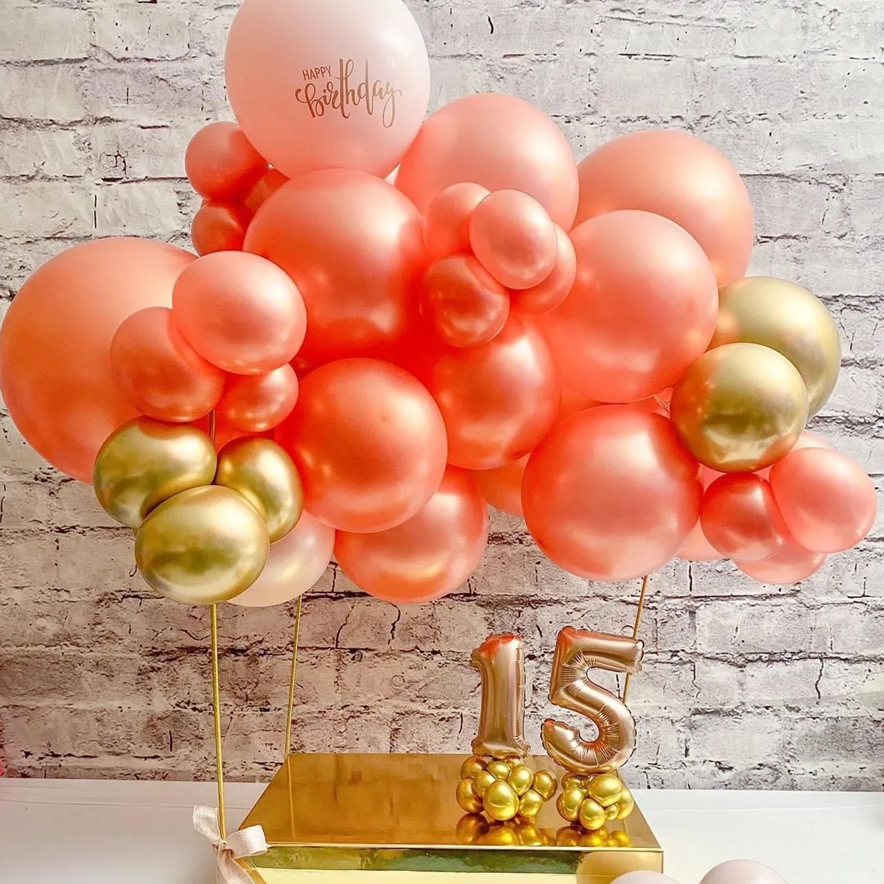 A cake topped with coral and gold balloons celebrating a 15th birthday.
